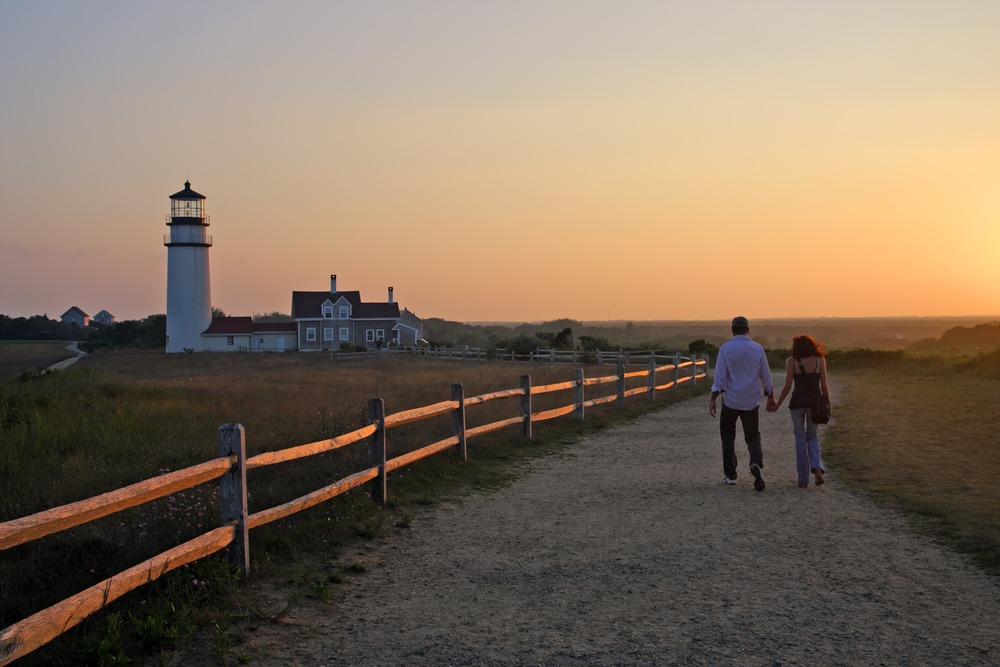couple walking on beach towards lighthouse at sunset